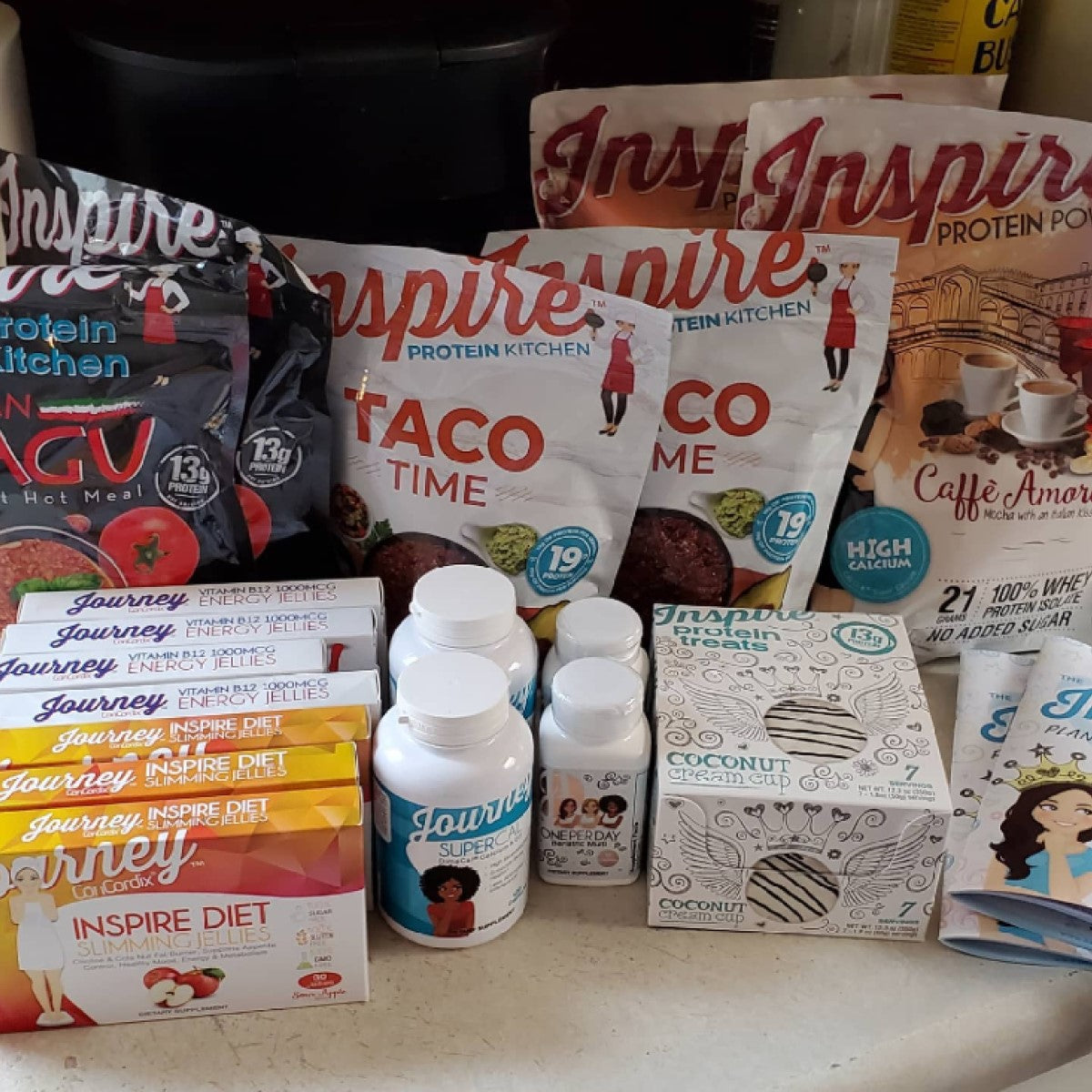 A variety of bariatric products is displayed on a countertop, including Inspire protein meals, Journey dietary supplements, and Inspire protein treats, showcasing options for healthy eating.