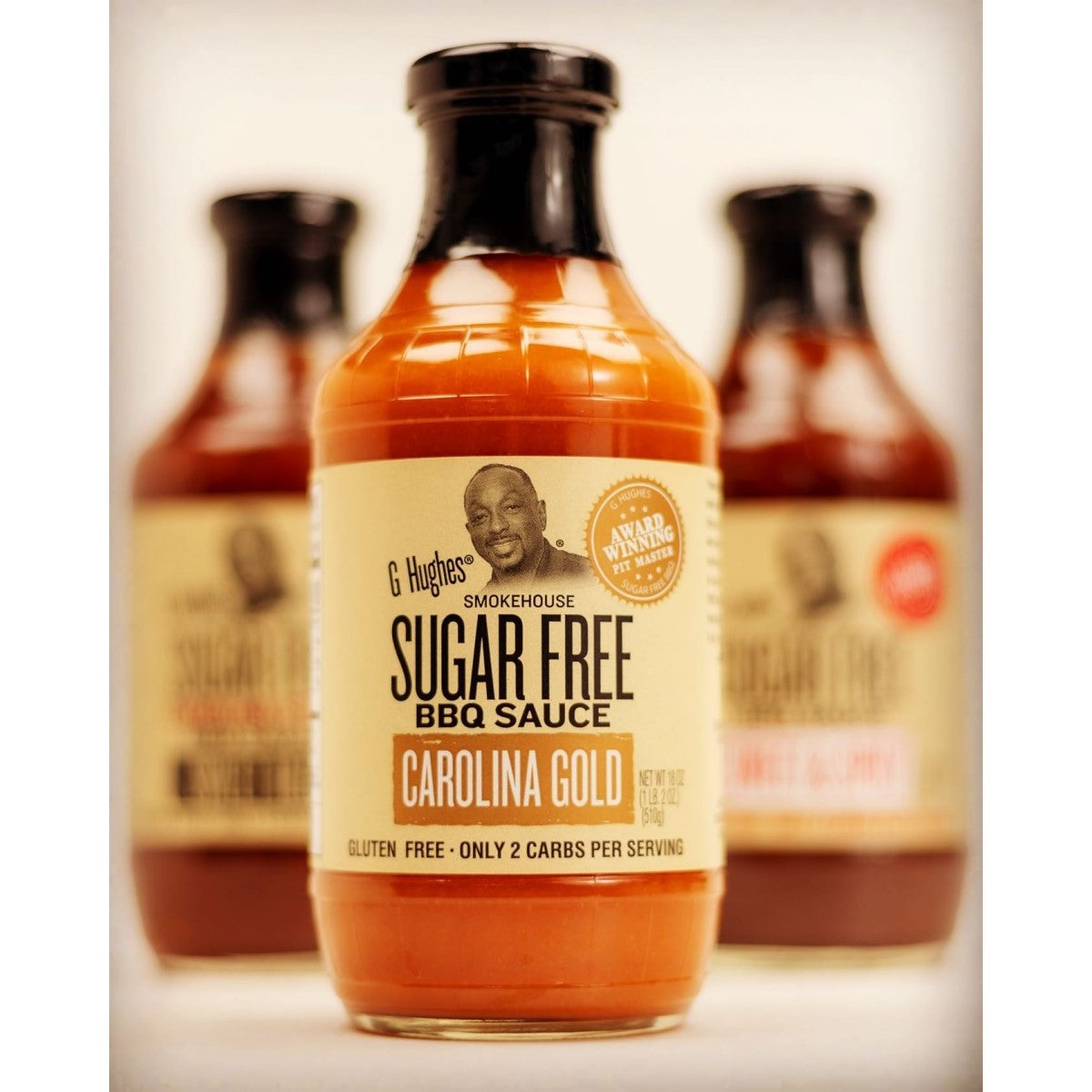 Three bottles of G Hughes Sugar Free BBQ Sauce are displayed, with the front bottle labeled "Carolina Gold," featuring a smiling man on the label and highlighting its gluten-free and low-carb attributes.