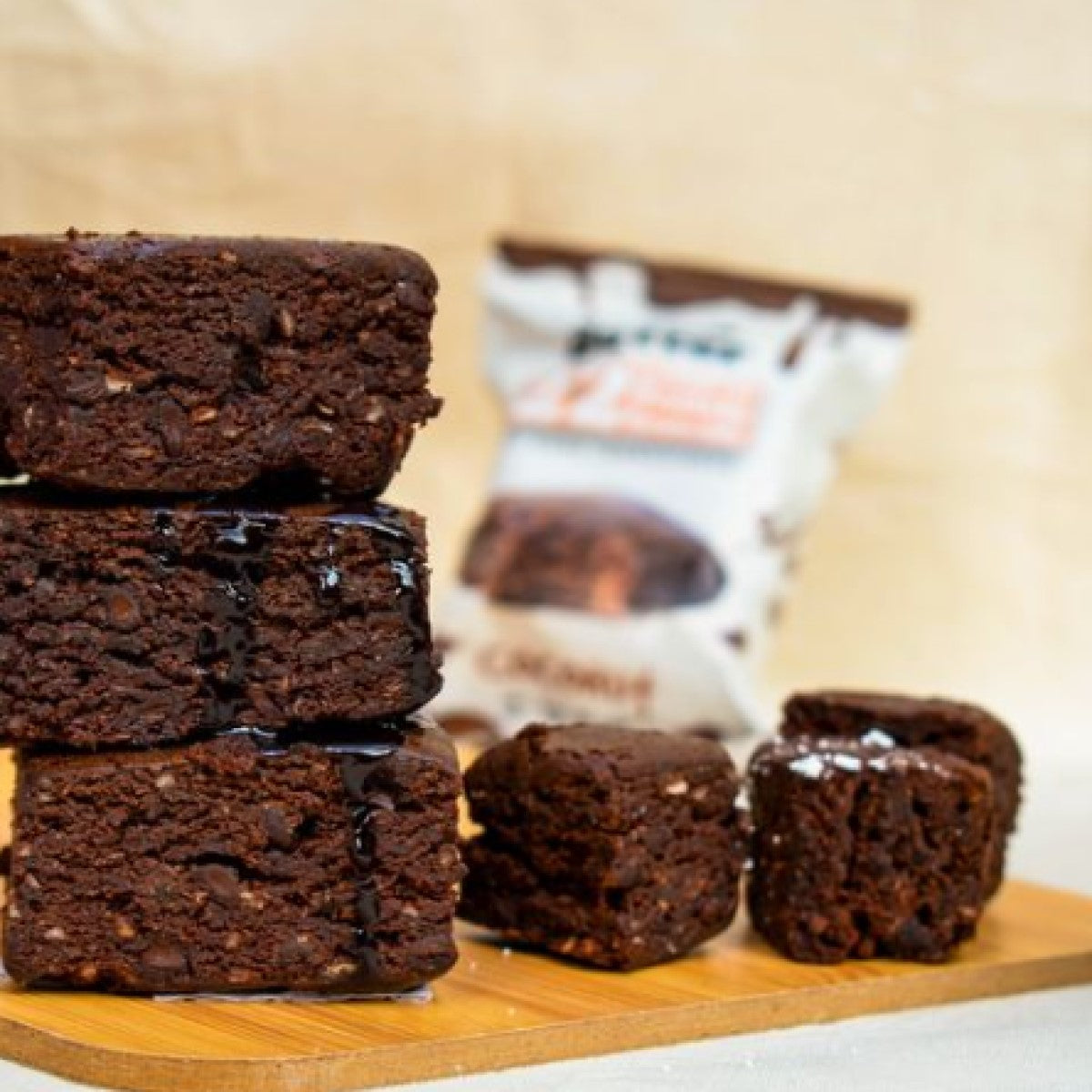 A stack of rich, chocolatey snack bars is displayed on a wooden board, with a smaller bar beside it, and a bag of Munch Better snacks partially visible in the background.