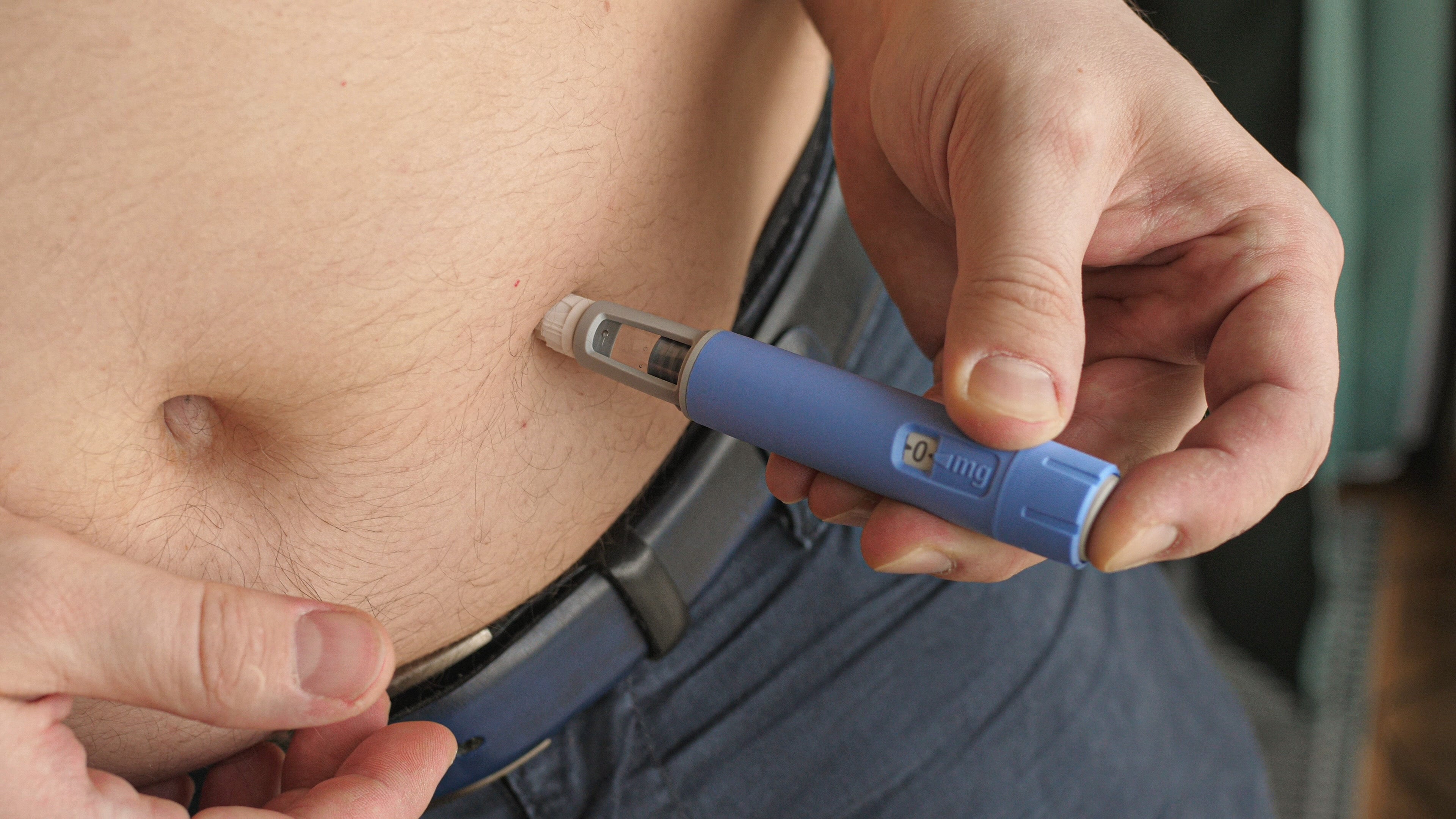 A person is injecting a weight loss medication into their abdomen using a blue pen-like device, highlighting the practical use of modern weight loss treatments.