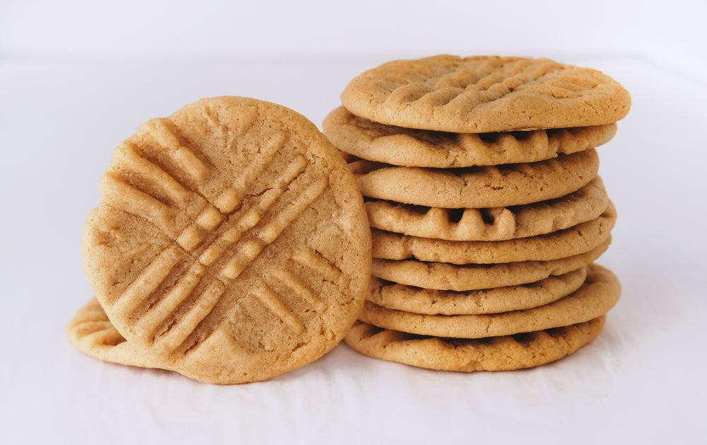 A stack of golden-brown peanut butter cookies is shown, with one cookie leaning against the pile, featuring a crisscross pattern on top.