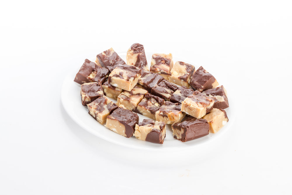 A white plate holds several pieces of chocolate peanut butter fudge, showcasing a mix of creamy and chocolate layers, arranged neatly and ready to be served.