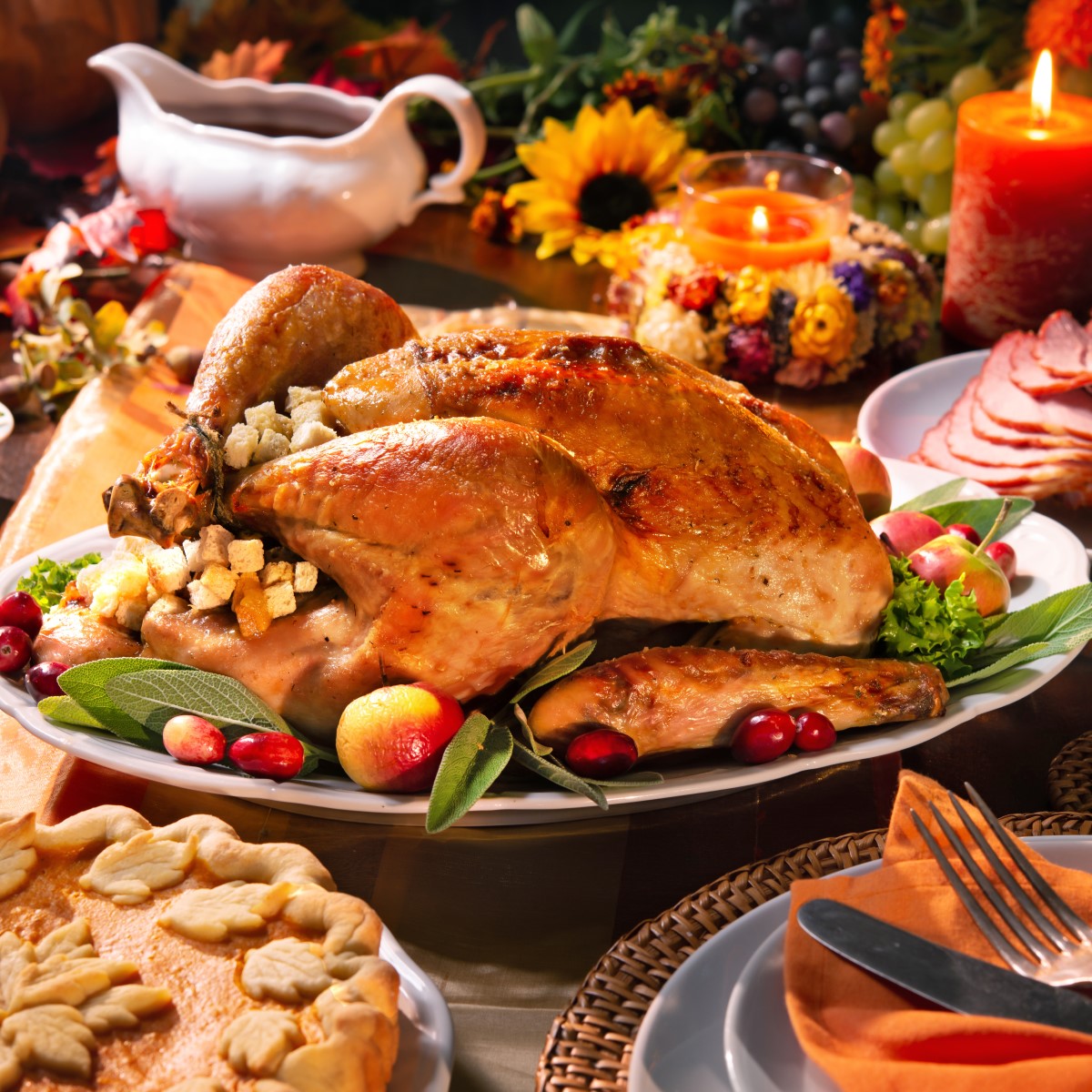 A beautifully roasted turkey garnished with herbs and fruits is the centerpiece of a festive Thanksgiving table, surrounded by colorful side dishes, candles, and autumn decorations.