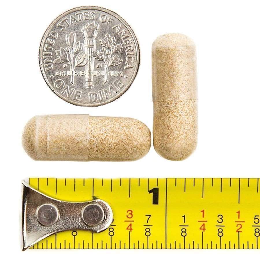 Three veggie gelatin capsules in a beige color are positioned near a dime and a measuring tape, highlighting their size and context for bariatric surgery multivitamin recommendations.