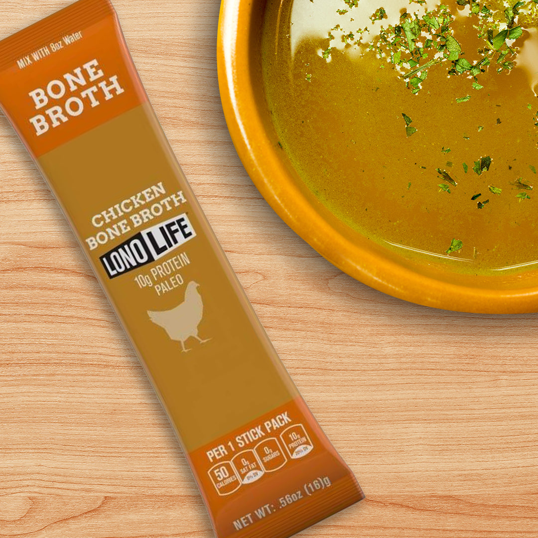 A packet of Lono Life chicken bone broth sits next to a bowl of golden broth garnished with herbs, all placed on a wooden surface, highlighting a nutritious option for the bariatric liquid stage.
