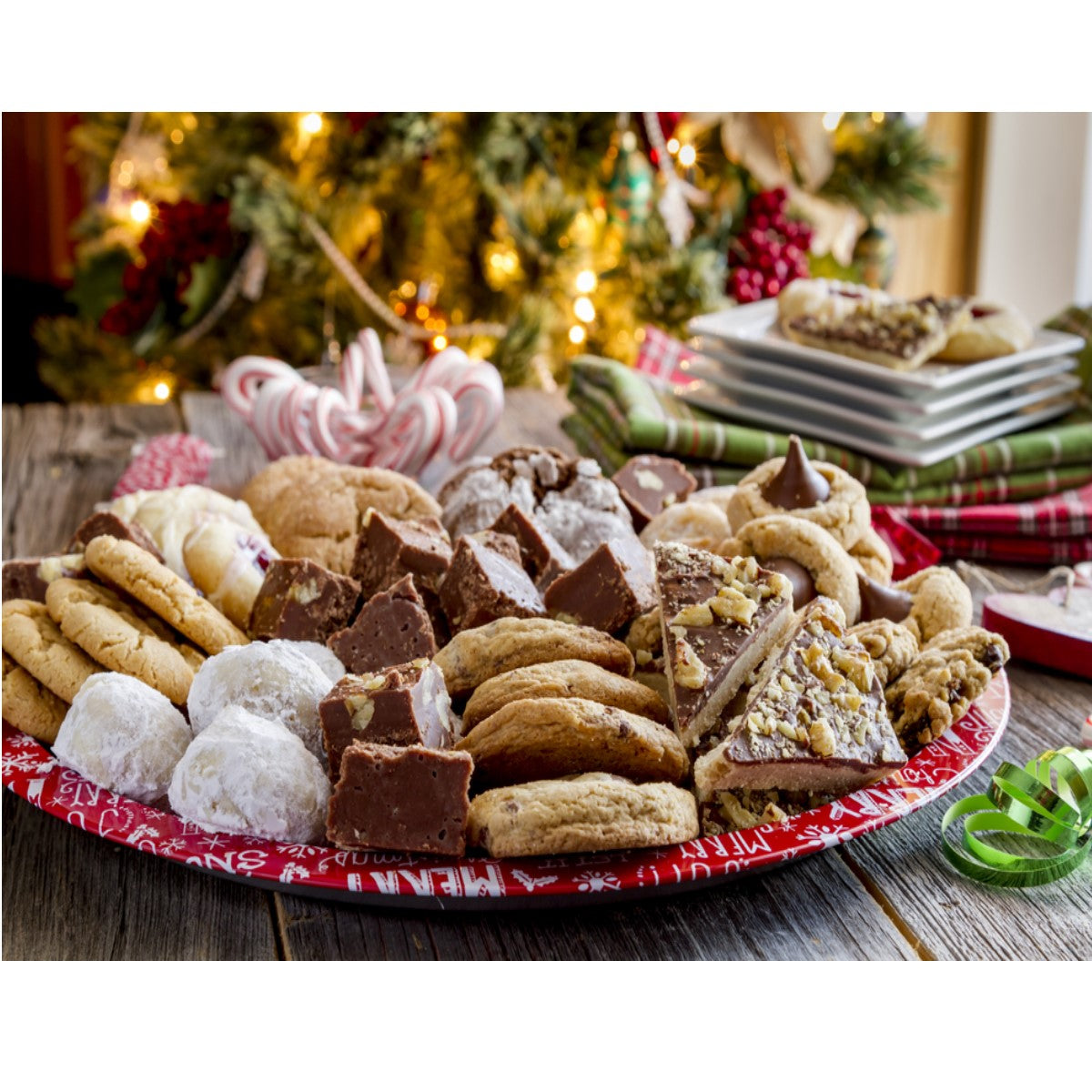 A festive platter filled with various bariatric-friendly desserts, including cookies and fudge, is displayed on a rustic wooden table, with a decorated Christmas tree and holiday decorations in the background.