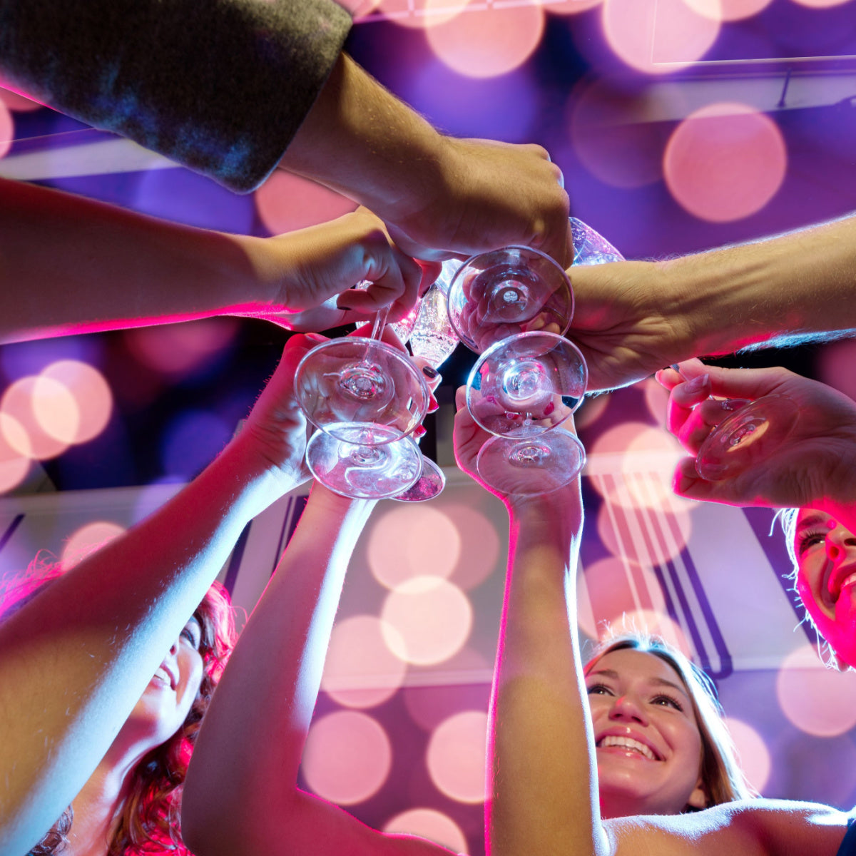 A group of people joyfully clink glasses together in a festive setting with colorful lights, celebrating with drinks, highlighting social interaction after bariatric surgery.