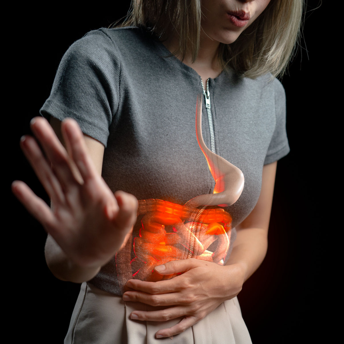 A woman in a gray top holds her stomach with one hand while the other hand is raised, showing a glowing, transparent representation of her digestive system against a dark background.