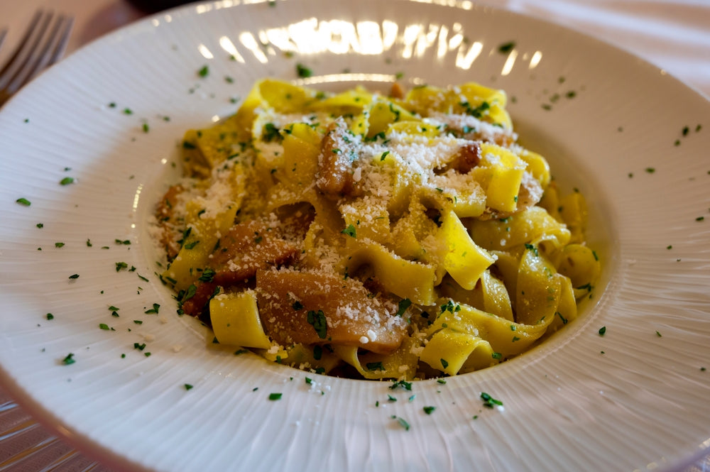 A plate of fettuccine pasta topped with grated cheese and sprinkled with green herbs sits on a white, textured dish, suggesting a delicious yet mindful dinner option for weight loss.