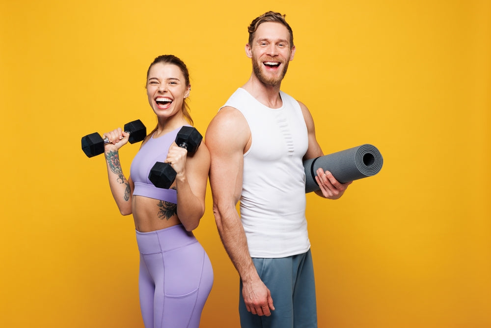A smiling woman in a purple workout outfit holds dumbbells, while a man in a white tank top and gray shorts holds a yoga mat, both posing against a bright yellow background.