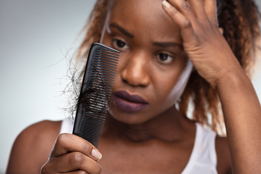 A woman looks concerned while holding a comb with hair strands stuck in it, reflecting on hair loss, possibly related to her experience after bariatric surgery.