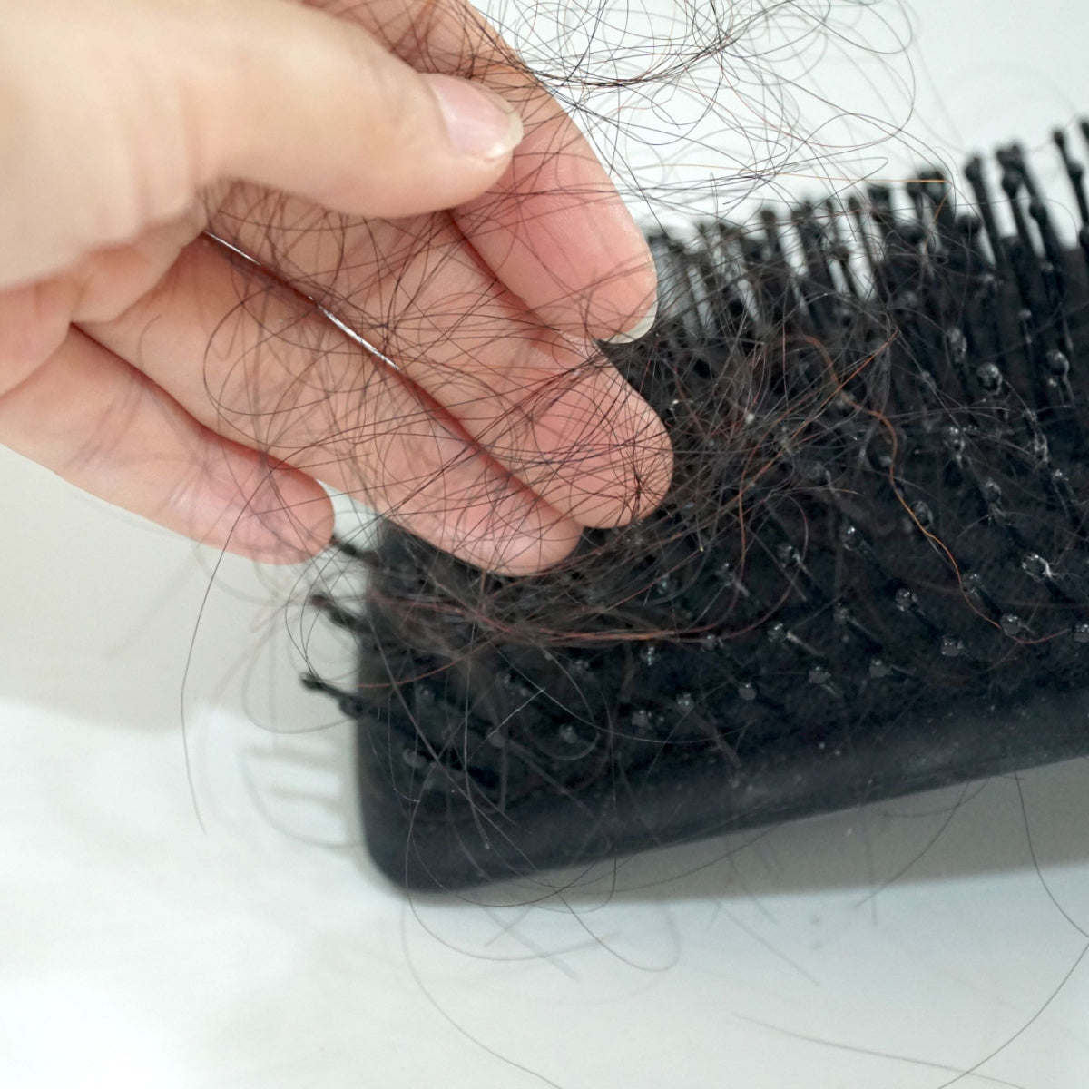 A hand holds strands of hair above a black hairbrush, which is covered with loose hair, highlighting concerns about hair loss after bariatric surgery.