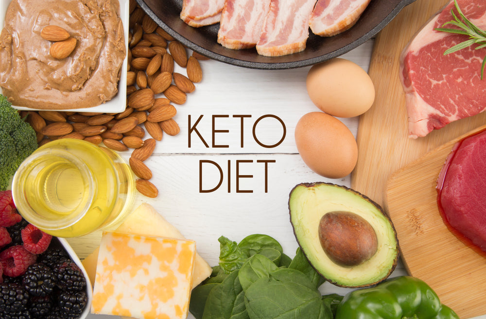 A variety of keto diet foods, including meats, eggs, nuts, vegetables, and oils, are arranged around the text "KETO DIET" on a wooden surface.
