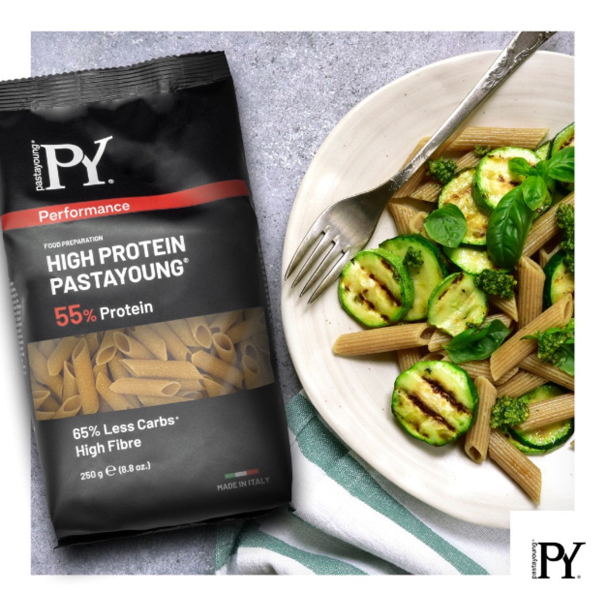 A package of high-protein pasta sits next to a plate of whole grain pasta mixed with grilled zucchini, broccoli, and fresh basil, showcasing a healthy meal option.