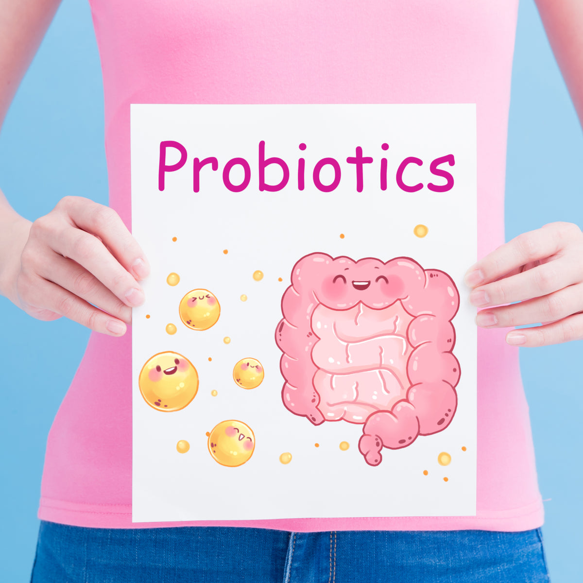 A person in a pink shirt holds a sign that says "Probiotics," featuring a smiling cartoon intestine and cheerful yellow bacteria against a light blue background.