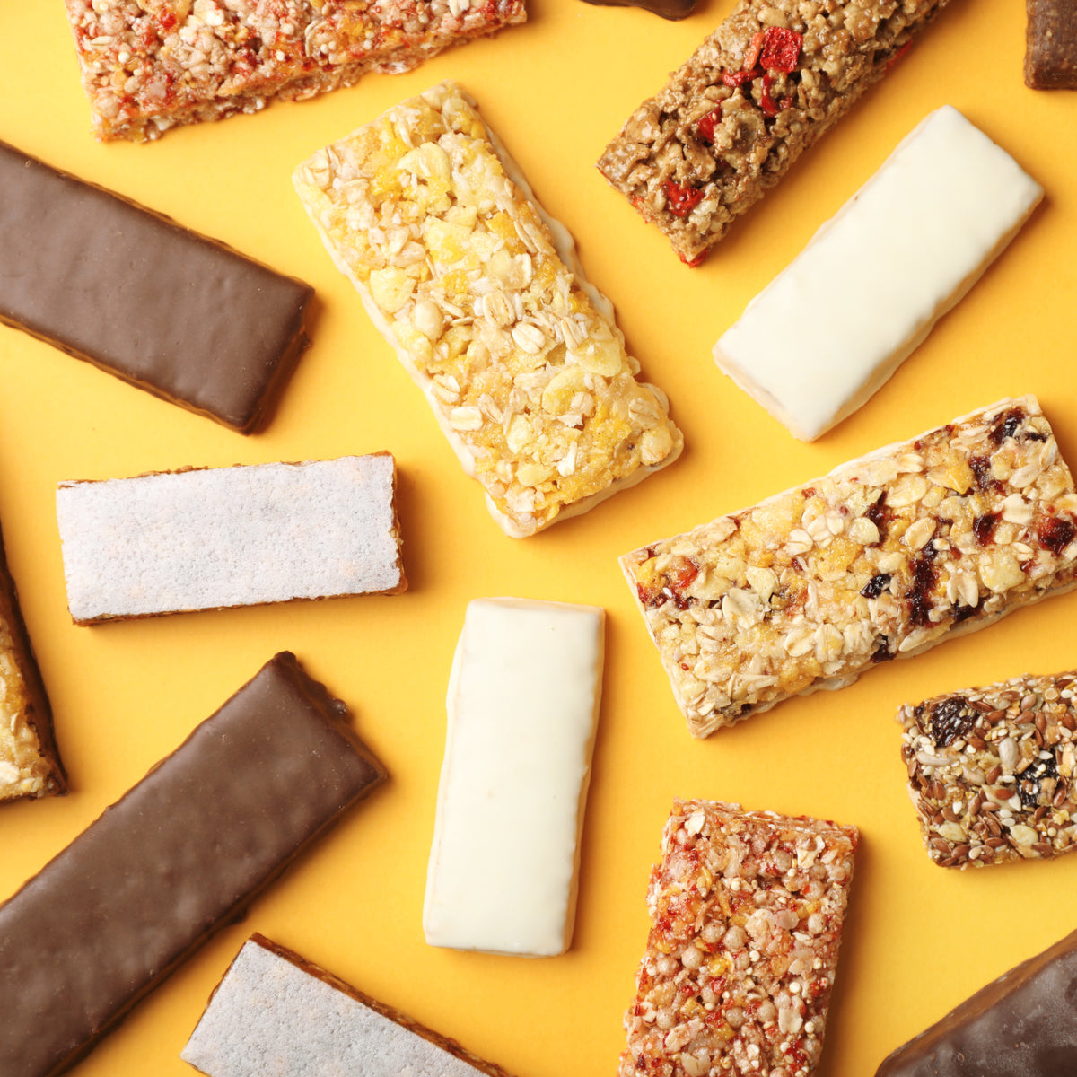 A variety of protein bars in different flavors and coatings are arranged on a bright yellow background, showcasing their textures and colors.
