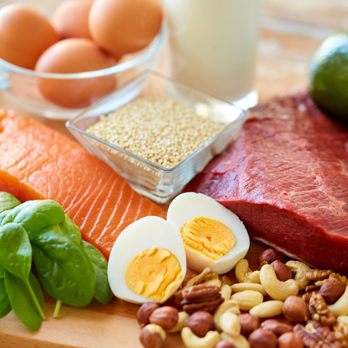 A variety of protein-rich foods, including salmon, beef, eggs, spinach, nuts, and quinoa, are arranged on a wooden surface, emphasizing their importance for nutrition after bariatric surgery.