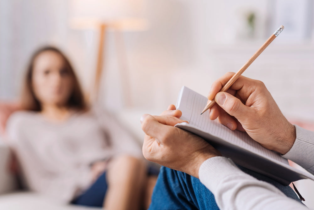 A therapist takes notes while listening to a patient, who is seated on a couch in a cozy, well-lit room, highlighting the importance of psychological support after bariatric surgery.