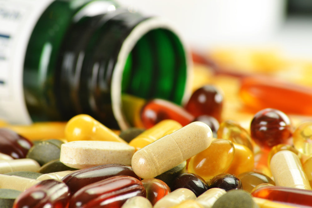 A variety of vitamins and supplements in different shapes and colors are scattered around an overturned green bottle, emphasizing the importance of nutrition after bariatric surgery.