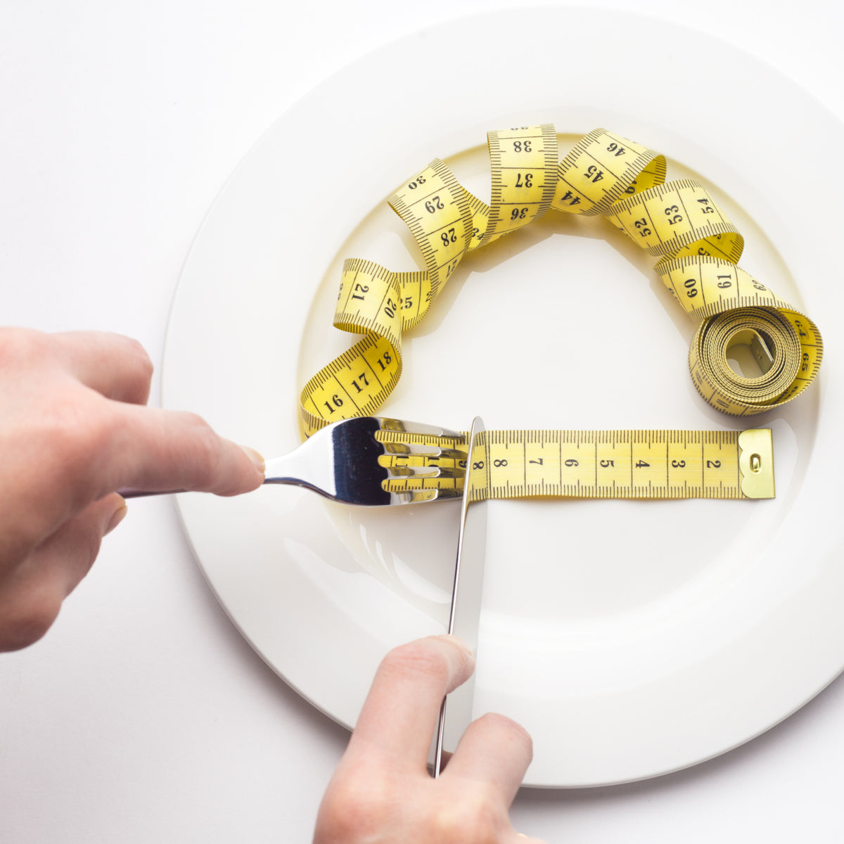 A hand holds a fork and knife, preparing to cut a yellow measuring tape coiled on a white plate, symbolizing a focus on portion control in the Pouch Reset Diet.