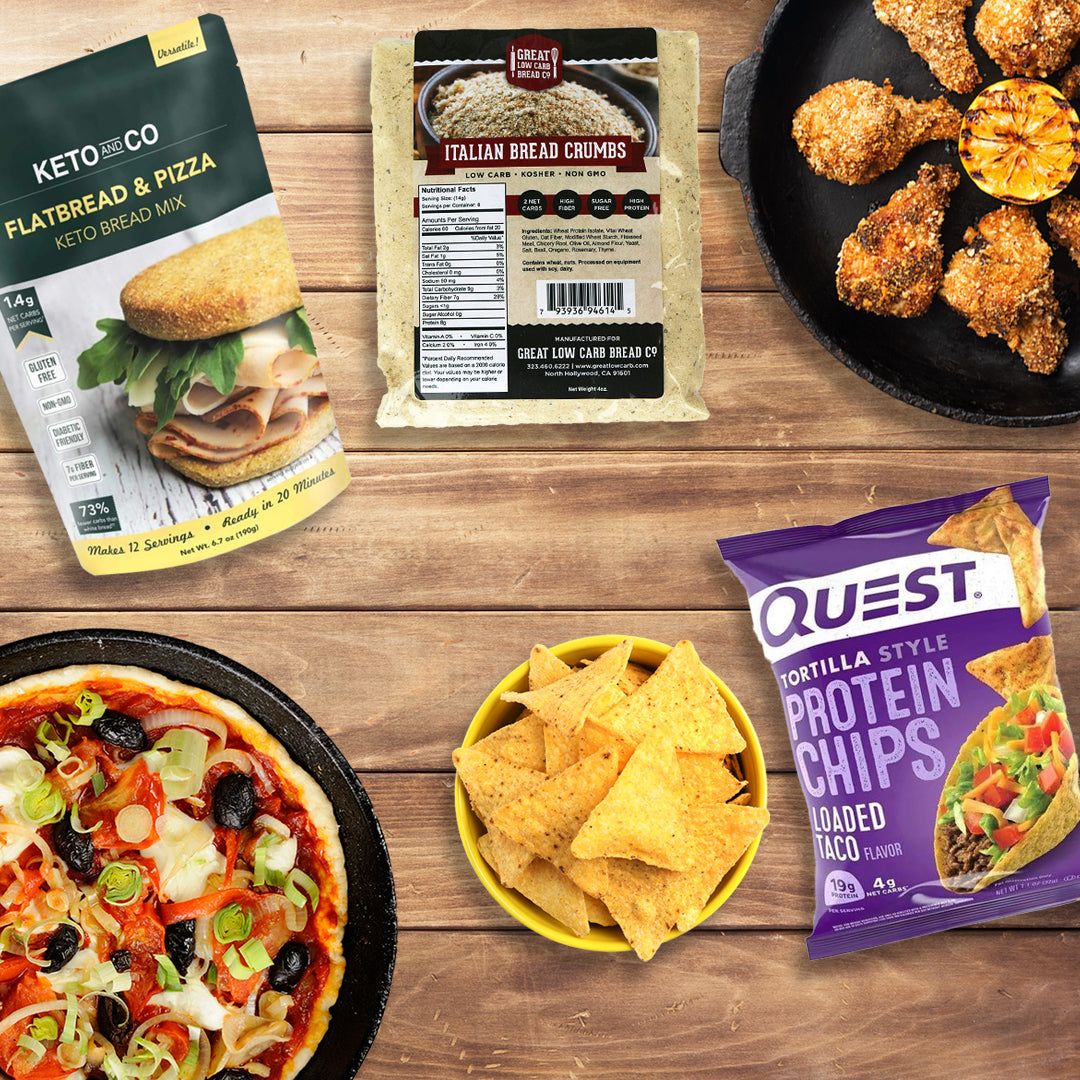 A variety of bariatric-friendly snacks for game day is displayed, including a keto flatbread mix, Italian bread crumbs, protein chips, and a pizza topped with vegetables and olives, all arranged on a wooden table.