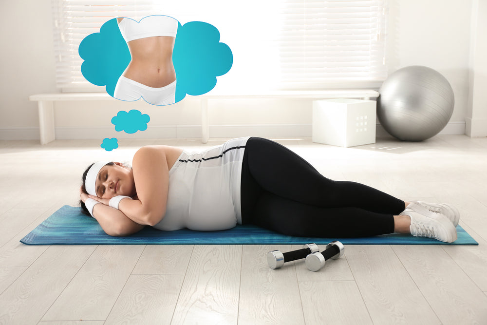 A person lies on a yoga mat in a bright room, resting with a thoughtful expression, while dreaming of a fit body, with dumbbells nearby and a fitness ball in the background.