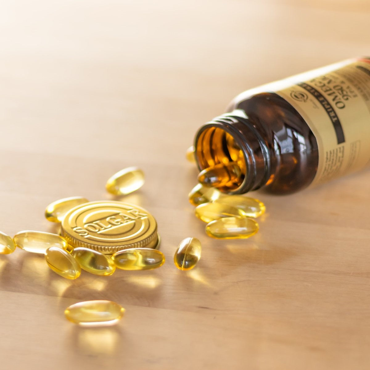 A brown bottle of SolgarĀ® vitamins is tipped over on a wooden surface, spilling several yellow gel capsules and revealing the gold cap with the Solgar logo.