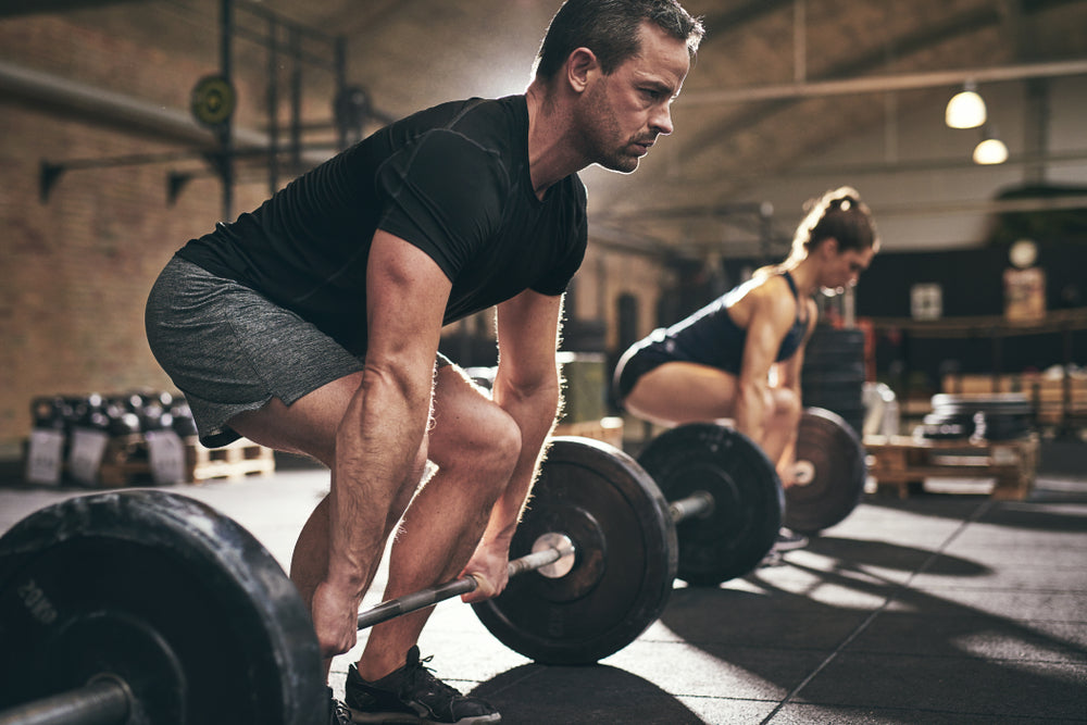 A man and a woman, both focused and determined, are performing deadlifts with heavy weights in a gym setting, emphasizing strength training after bariatric surgery.