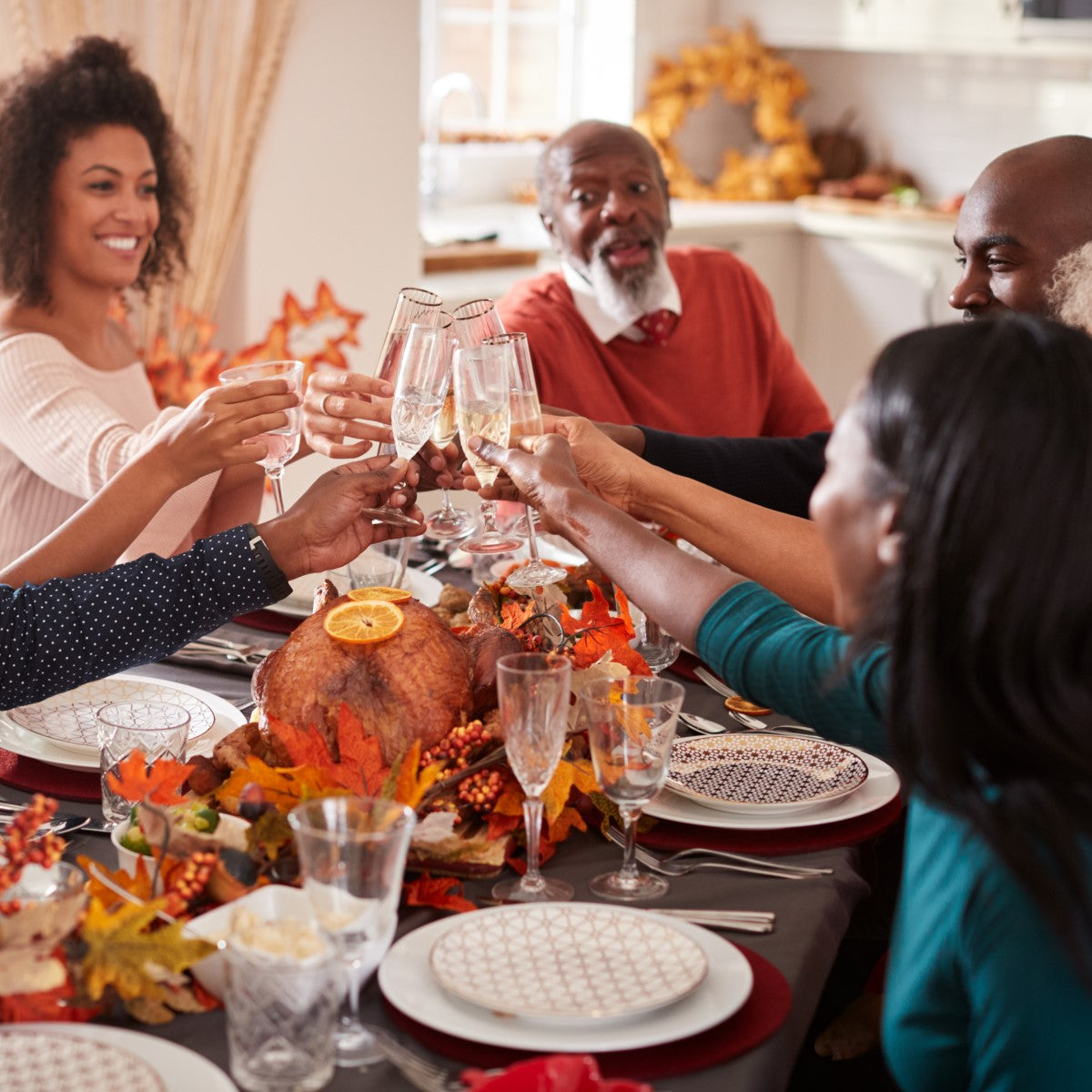 A diverse group of people joyfully toast with glasses at a Thanksgiving table adorned with a turkey and autumn decorations, celebrating together after bariatric surgery.