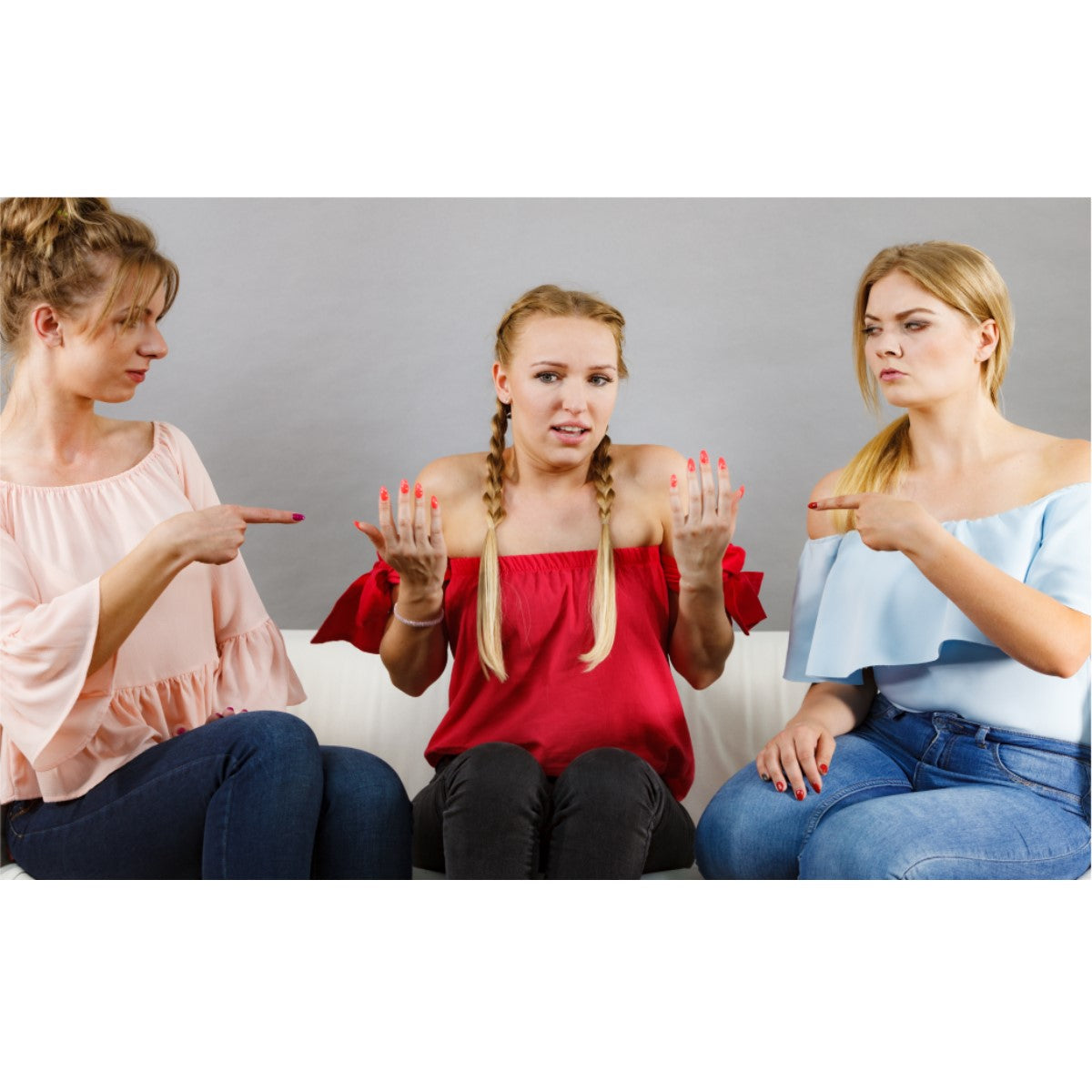 Three women sit on a couch; one in a red top looks confused with raised hands, while the others, in pink and blue tops, point at her with serious expressions, suggesting a discussion about weight loss comments.