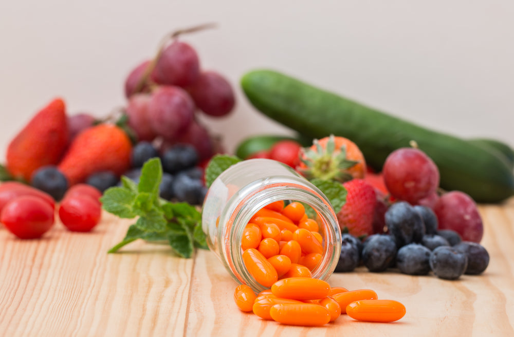 A glass jar spills bright orange vitamins onto a wooden surface, surrounded by fresh fruits like strawberries, blueberries, and grapes, emphasizing the importance of nutrients after bariatric surgery.