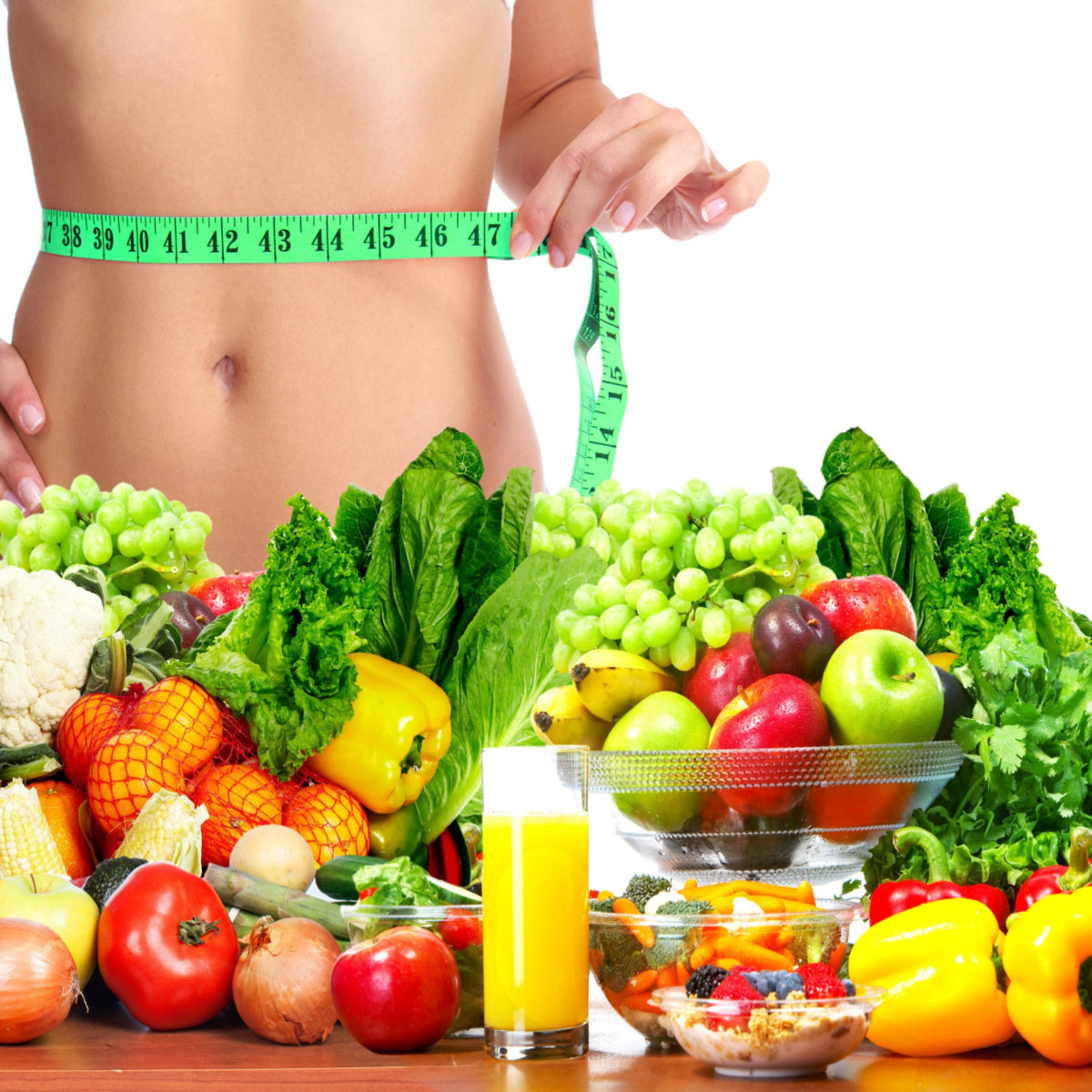 A person holds a measuring tape around their waist, surrounded by a variety of fresh fruits and vegetables, with a glass of orange juice and a bowl of mixed salad in the foreground.