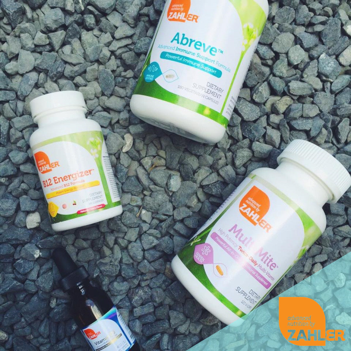 Four bottles of Zahler dietary supplements, including B12 Energizer, Abreve, and MultiMite, are arranged on a bed of gray gravel, showcasing their labels and branding.