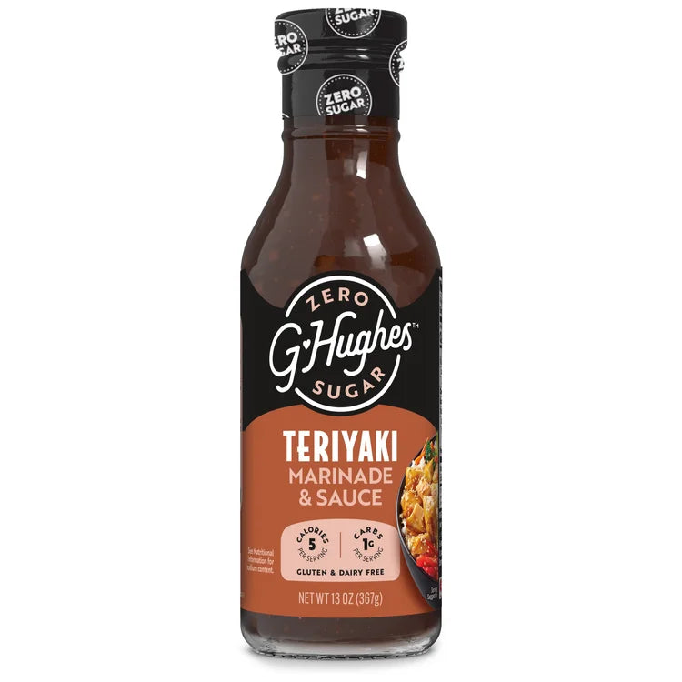 A clear glass bottle of G. Hughes Zero Sugar Teriyaki Marinade & Sauce, featuring a black label with white text, sits against a plain background, showcasing its gluten-free and low-calorie attributes.