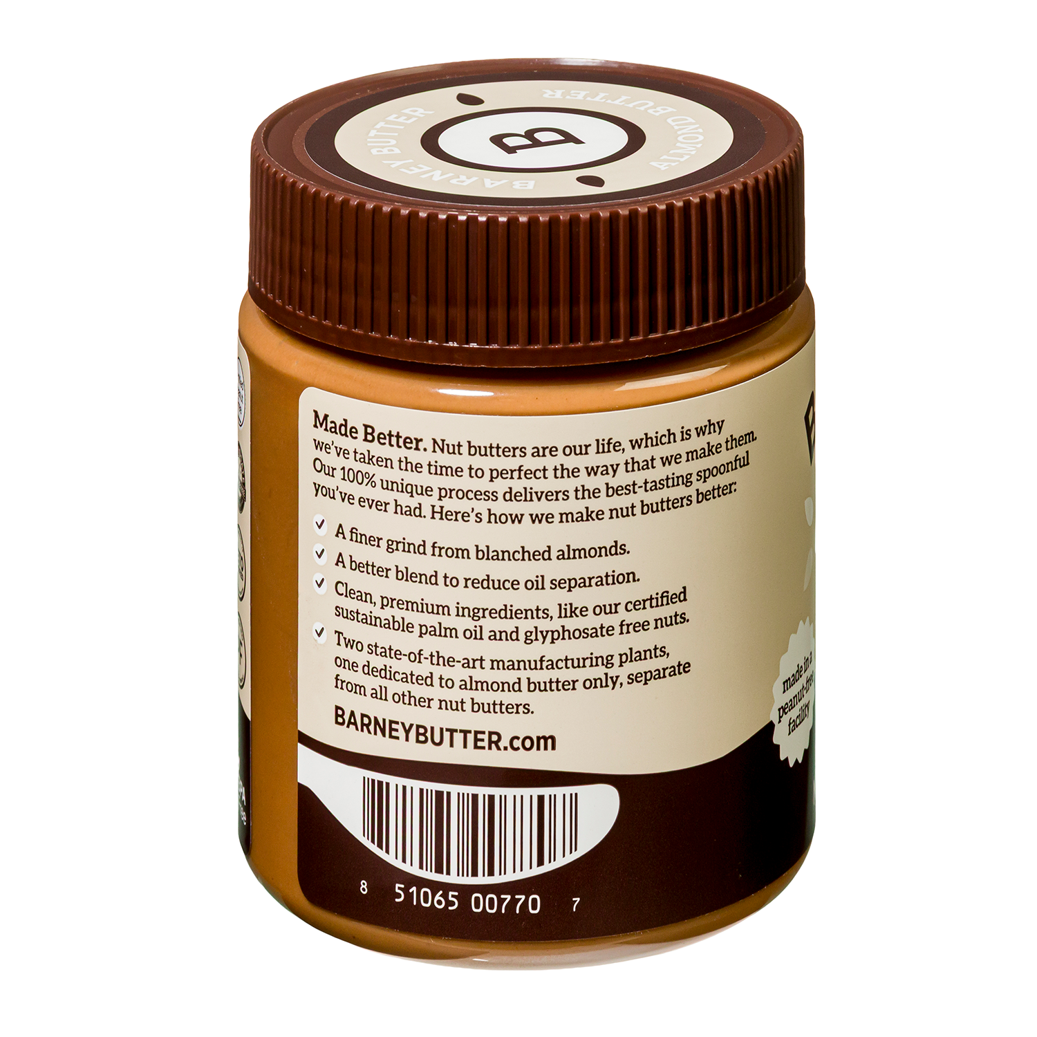 A jar of Barney Butter almond butter features a brown lid and a label detailing its premium ingredients and manufacturing process, emphasizing a smooth texture and reduced oil separation.