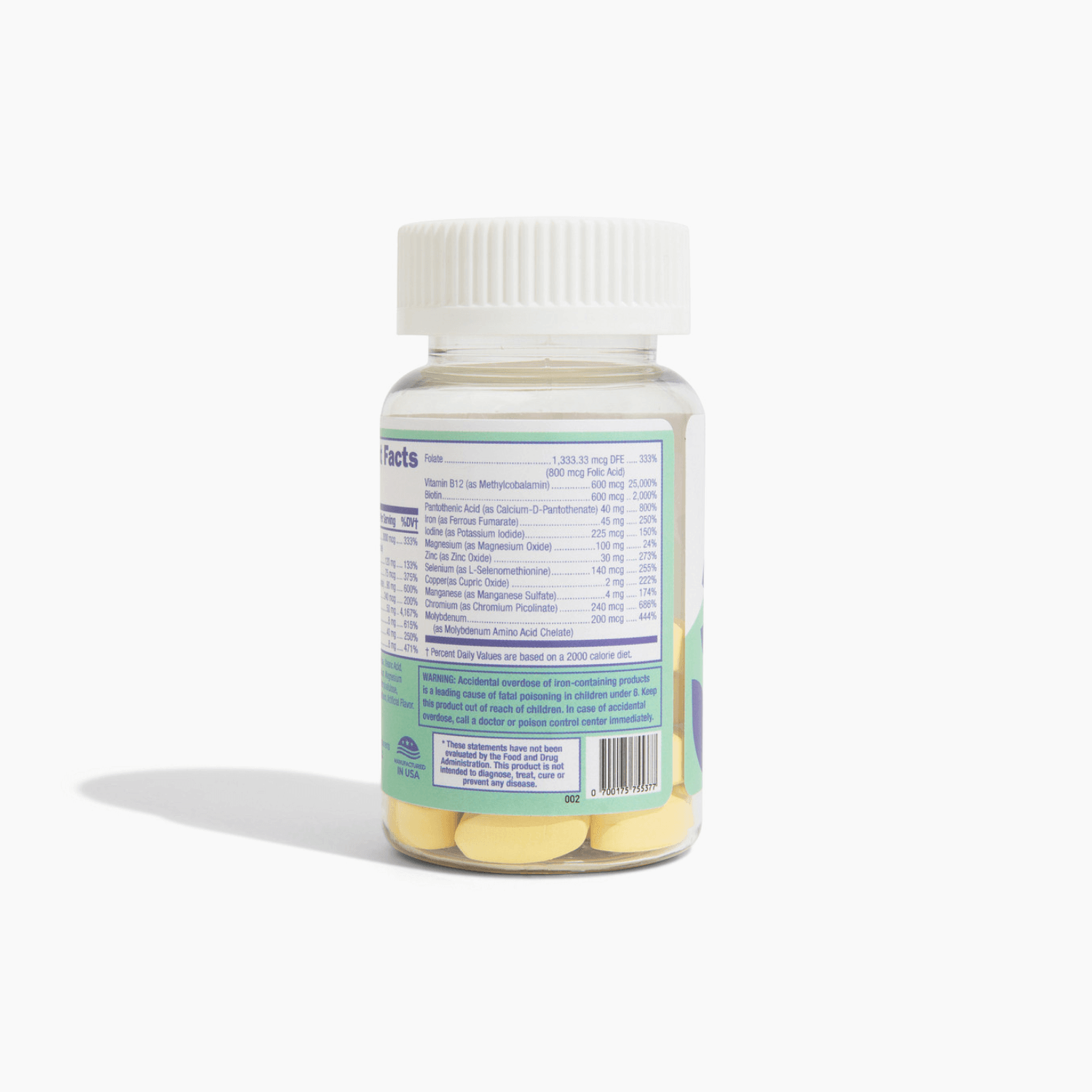 A clear plastic bottle with a white cap contains yellow vitamins, displaying a nutrition facts label on the back with detailed ingredient information and a warning about iron overdose.