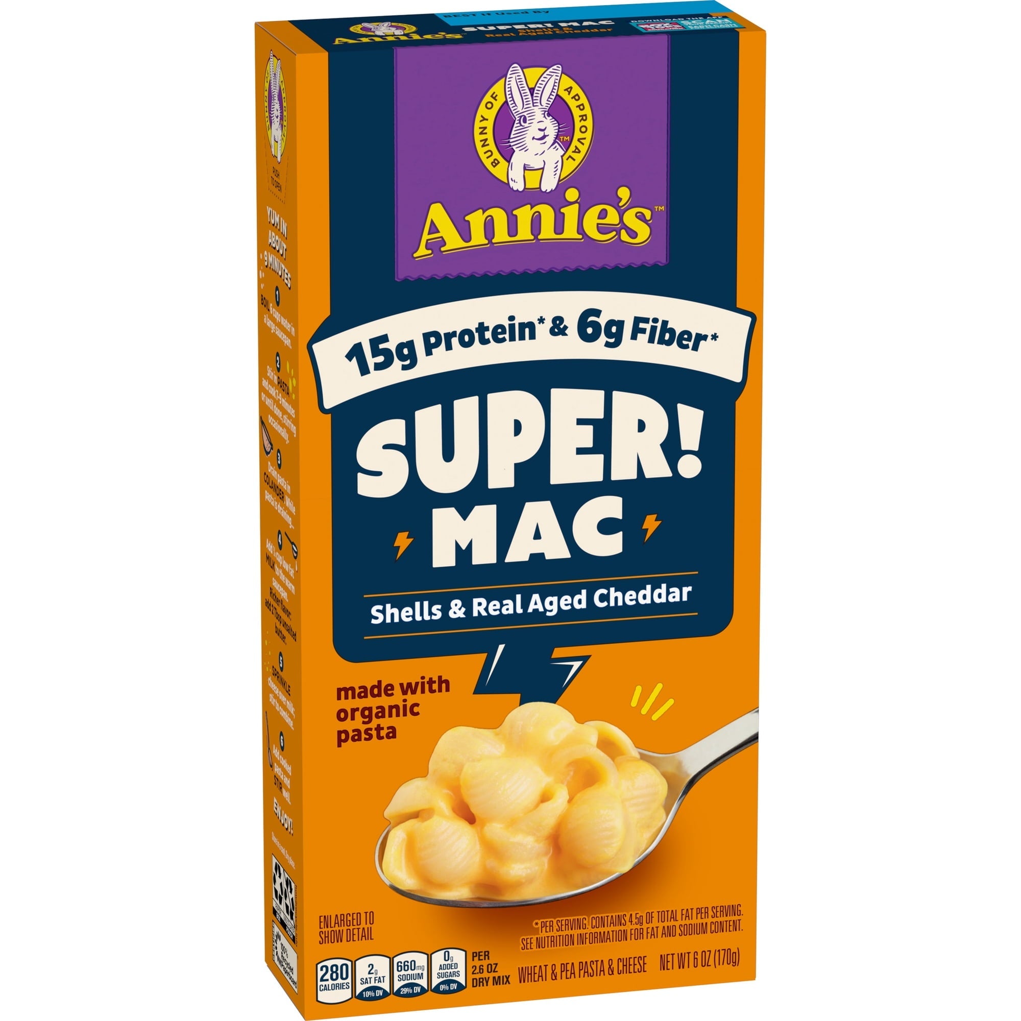 A brightly colored box of Annie's Super Mac features a spoonful of creamy macaroni and cheese, highlighting its 15g protein and 6g fiber, with a playful bunny logo at the top.