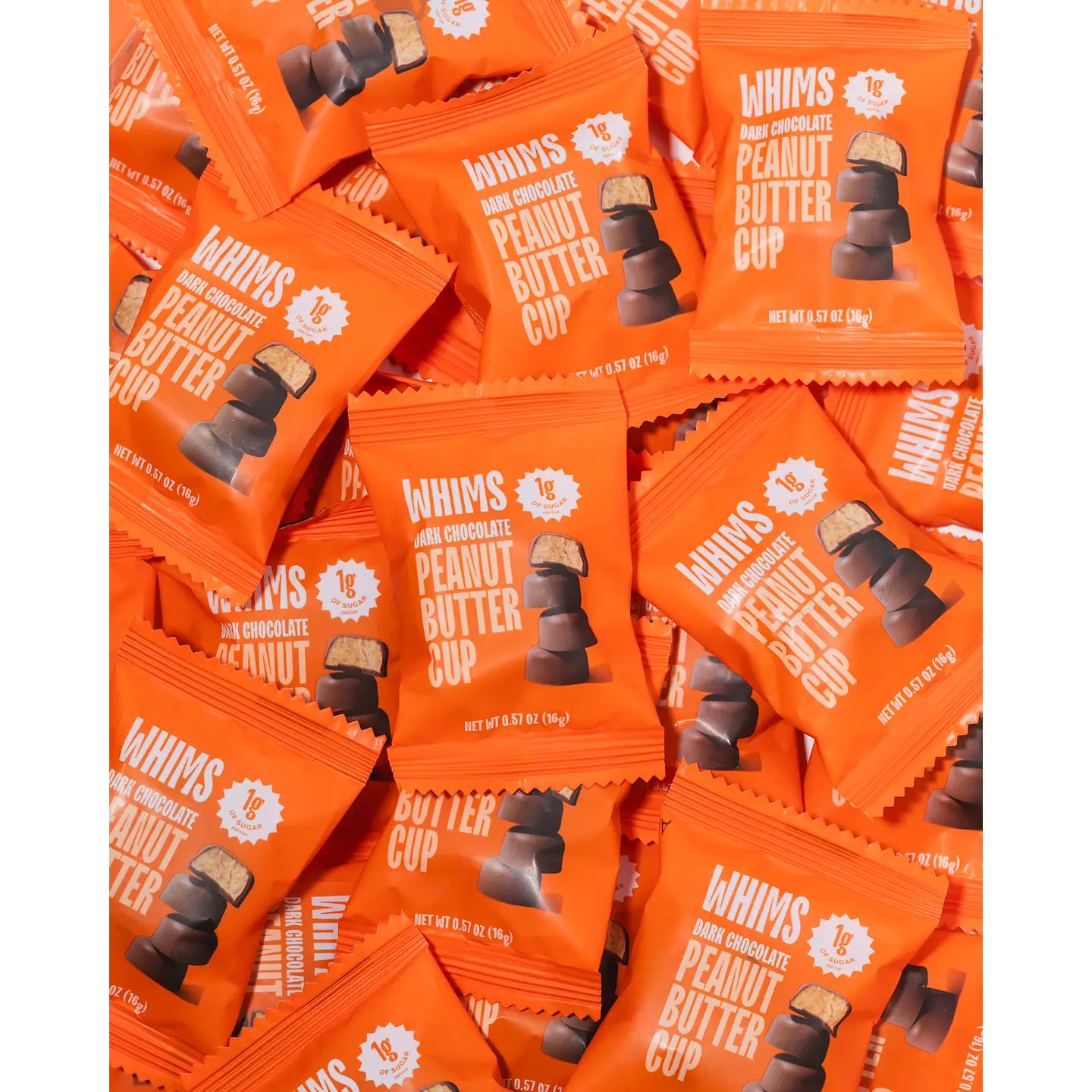 A pile of bright orange wrappers for WHIMS dark chocolate peanut butter cups, showcasing the product name and nutritional information prominently on each package.