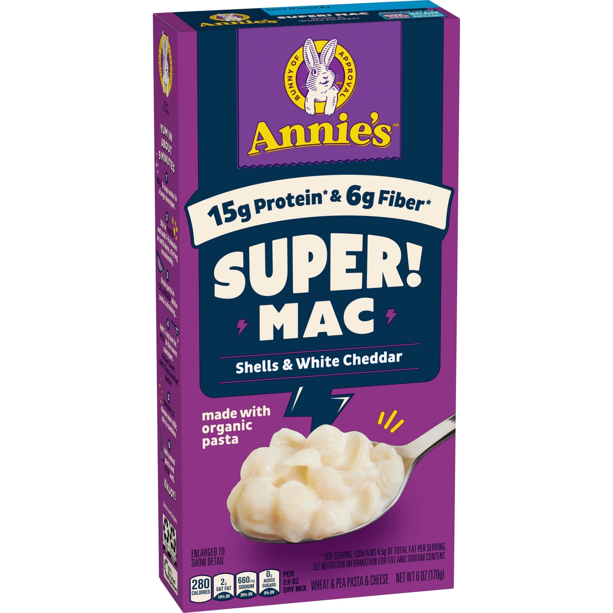 A purple box of Annie's Super Mac featuring shells and white cheddar, highlighting 15g of protein and 6g of fiber, with a spoonful of creamy pasta displayed in front.