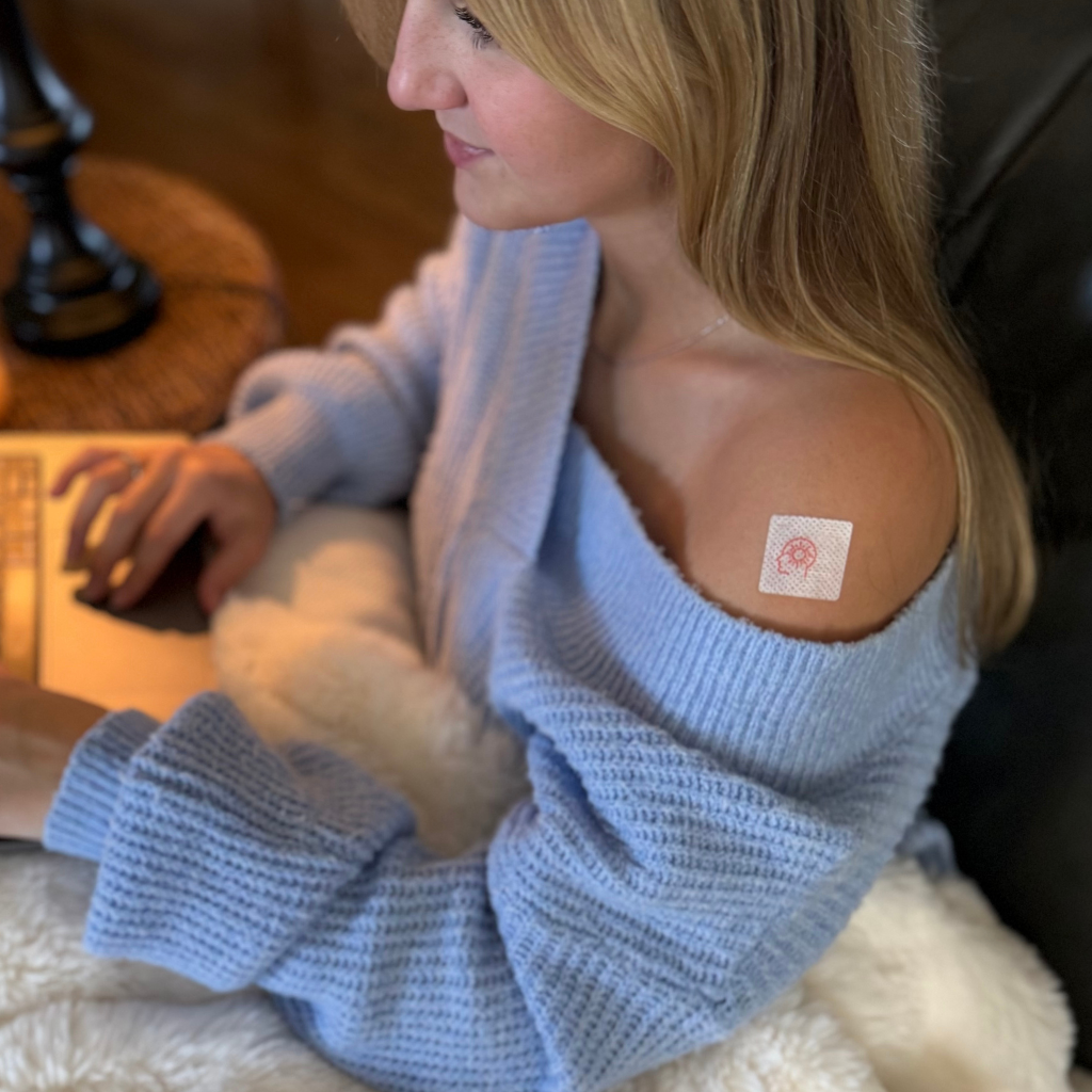 Woman wearing a light blue sweater with a visible tattoo on her arm, sitting indoors.