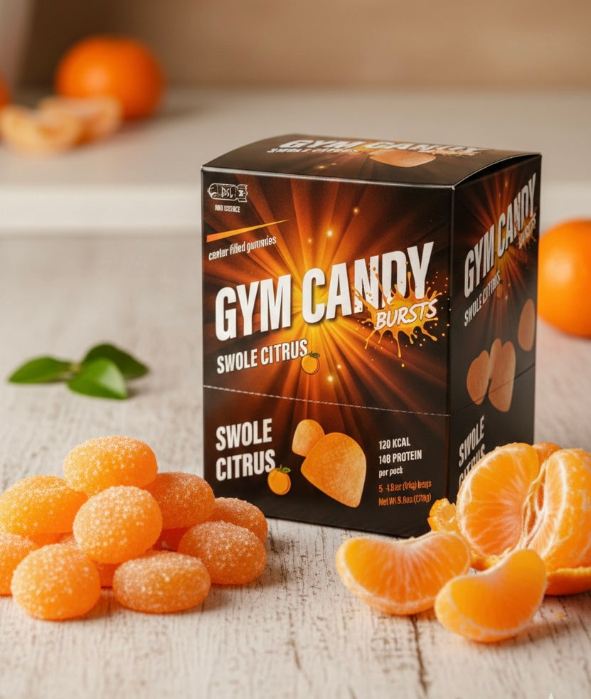 A box of "Gym Candy Bursts" in Swole Citrus flavor sits on a wooden surface, surrounded by orange gummy candies and fresh orange segments, highlighting a vibrant and energetic snack option.