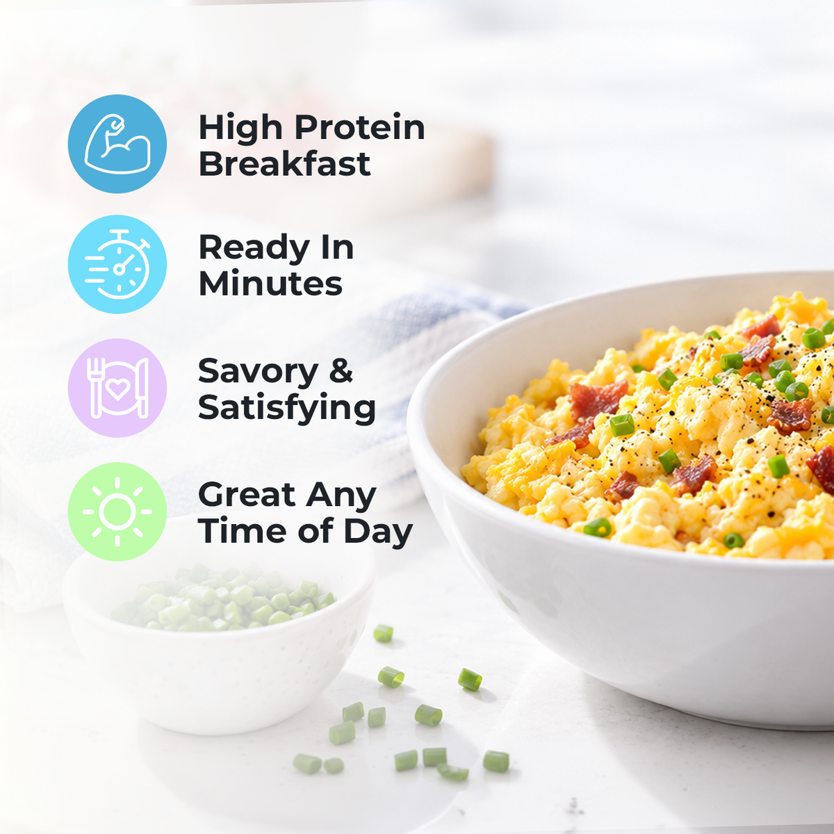 A bowl of fluffy scrambled eggs topped with green onions and bacon bits sits on a light countertop, accompanied by a small bowl of chopped green onions, highlighting a high-protein breakfast option.