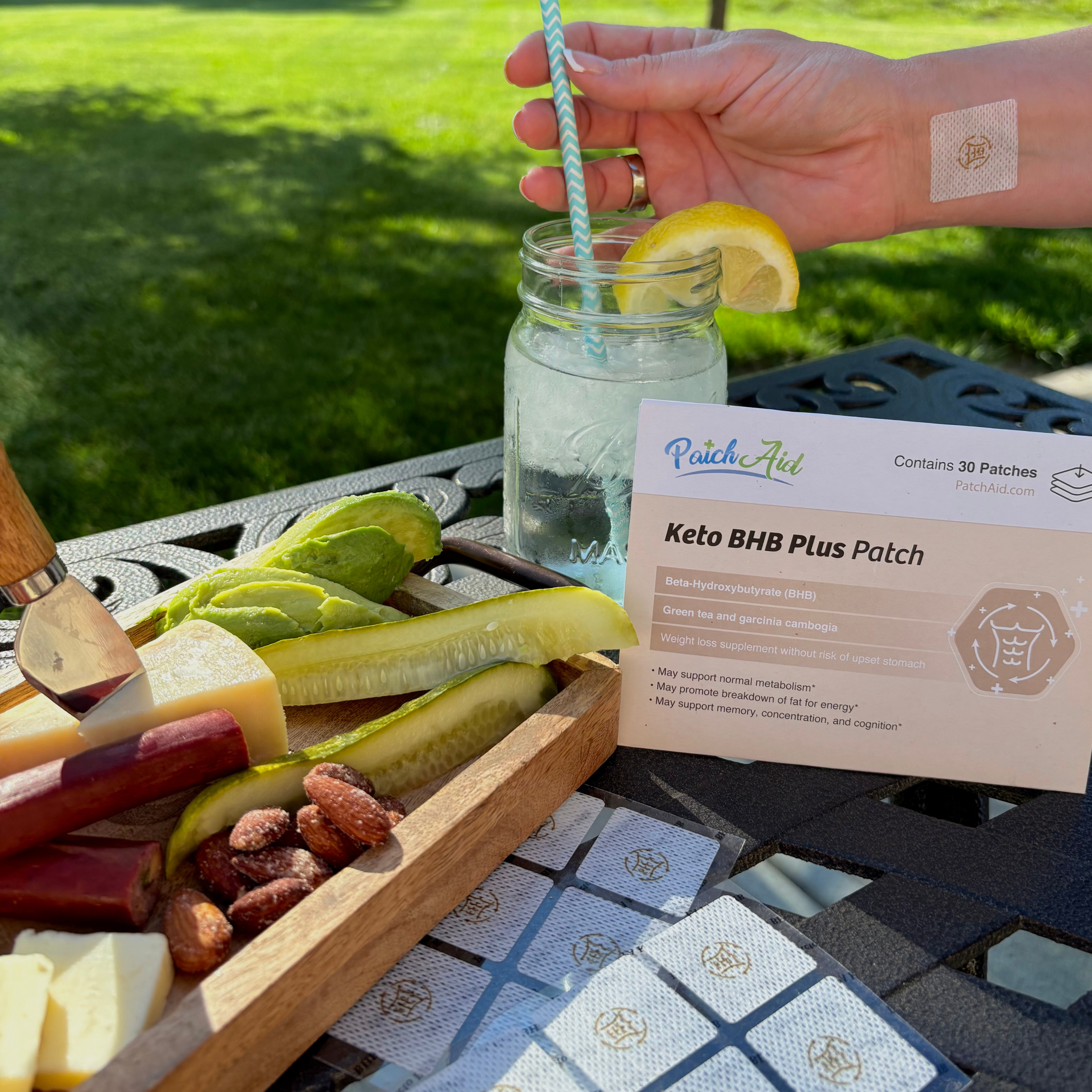 Mason jar with lemon slice, straw, and snack platter on a table outdoors.