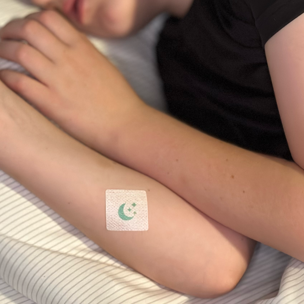 A child is resting with their arms crossed on a striped blanket, featuring a bandage with a moon and stars design on one arm.
