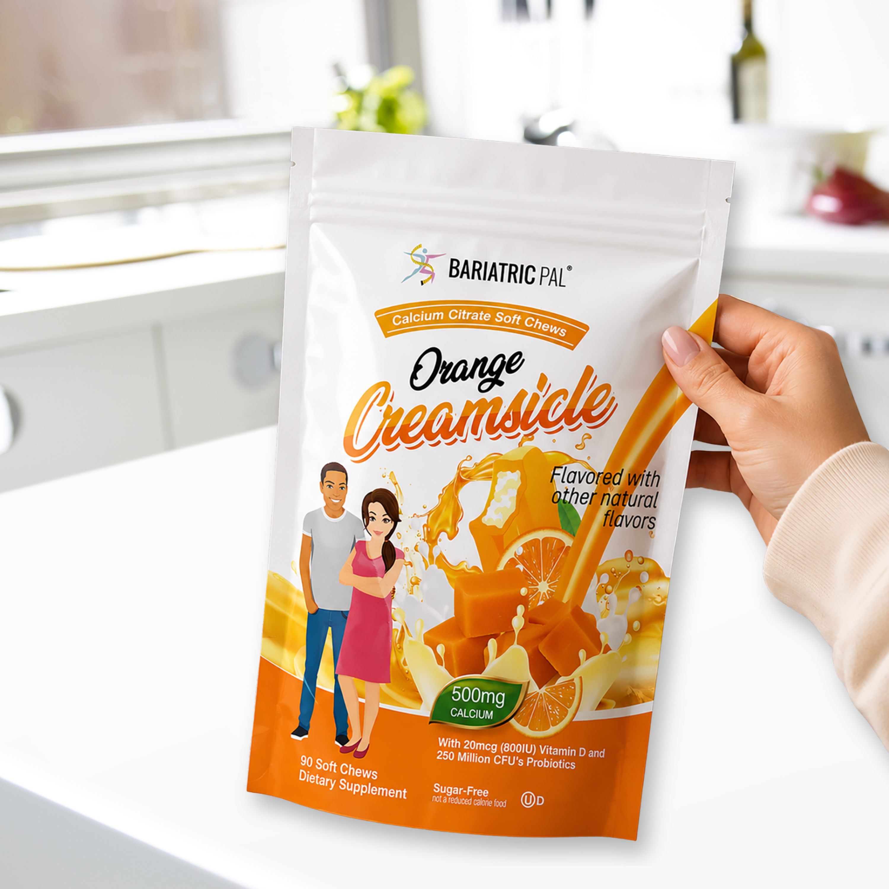 A hand holds a package of Bariatric Pal Orange Creamsicle calcium citrate soft chews, featuring illustrations of a man and woman, with a bright kitchen background.