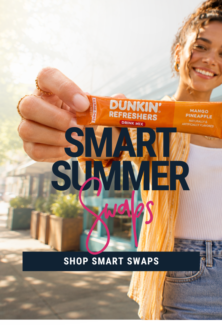A smiling woman holds a packet of Dunkin' Refreshers Mango Pineapple drink mix in a sunny outdoor setting, promoting "Smart Summer Swaps" with a vibrant background of greenery and shops.