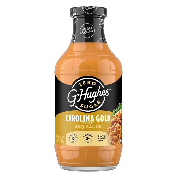 A clear bottle of G. Hughes Carolina Gold BBQ sauce displays a golden-orange sauce, with labels highlighting it as zero sugar, gluten-free, and low in calories, ideal for flavorful cooking.