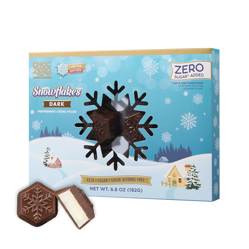 A box of ChocZero Snowflakes Dark chocolate, featuring peppermint crème filling, is displayed with one chocolate piece partially unwrapped, set against a winter-themed background with snowflakes.