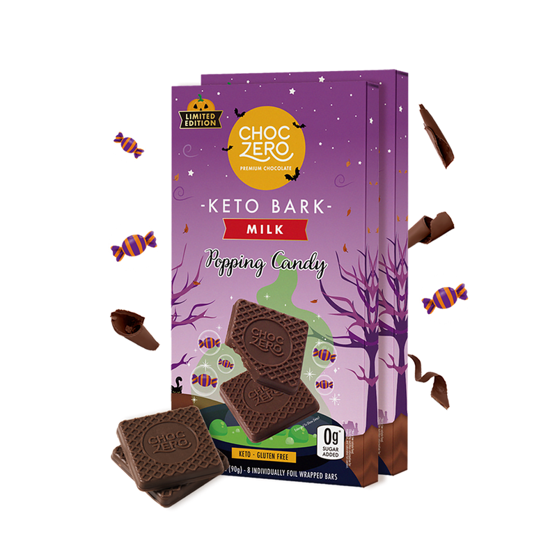 A colorful package of ChocZero Keto Bark Milk with popping candy features chocolate pieces in front, set against a whimsical purple background with Halloween-themed decorations.