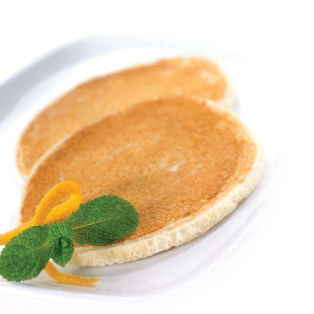 Two golden-brown pancakes are placed on a white plate, garnished with a sprig of fresh mint and a twist of orange peel.